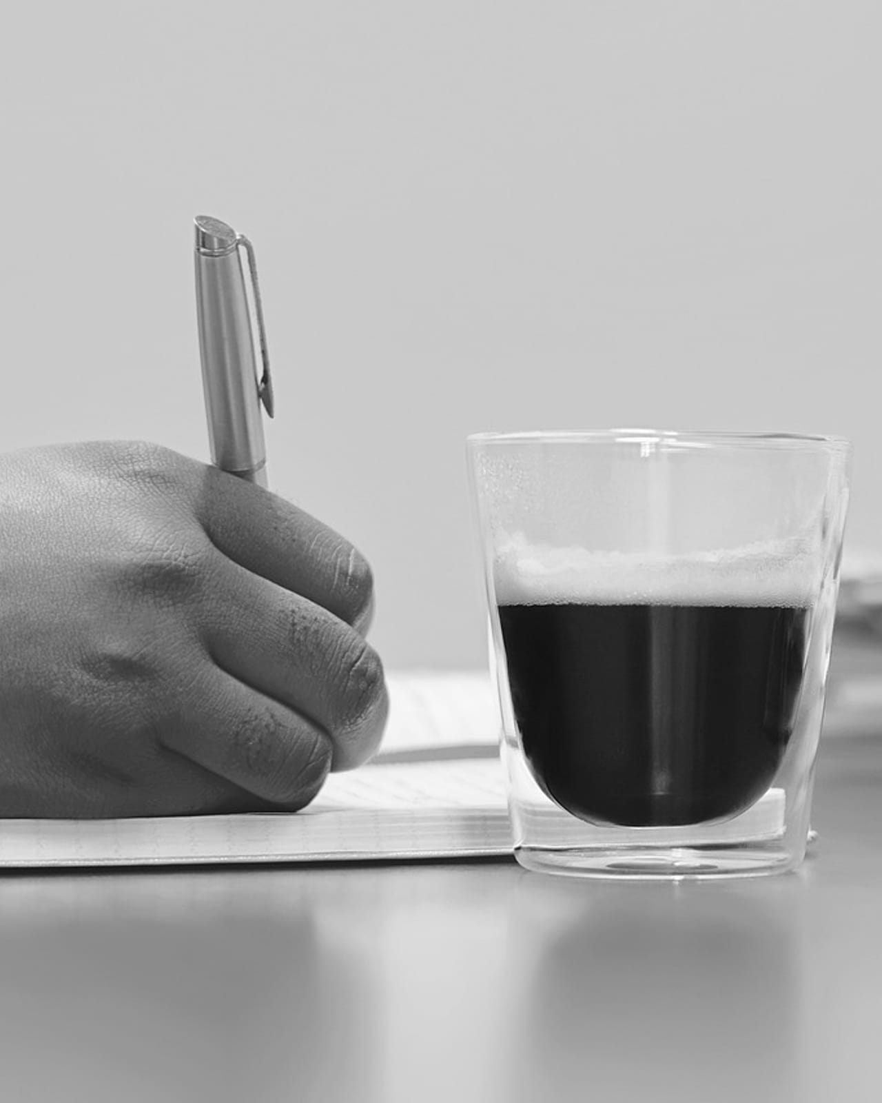A hand writing notes at a desk beside a cup of coffee